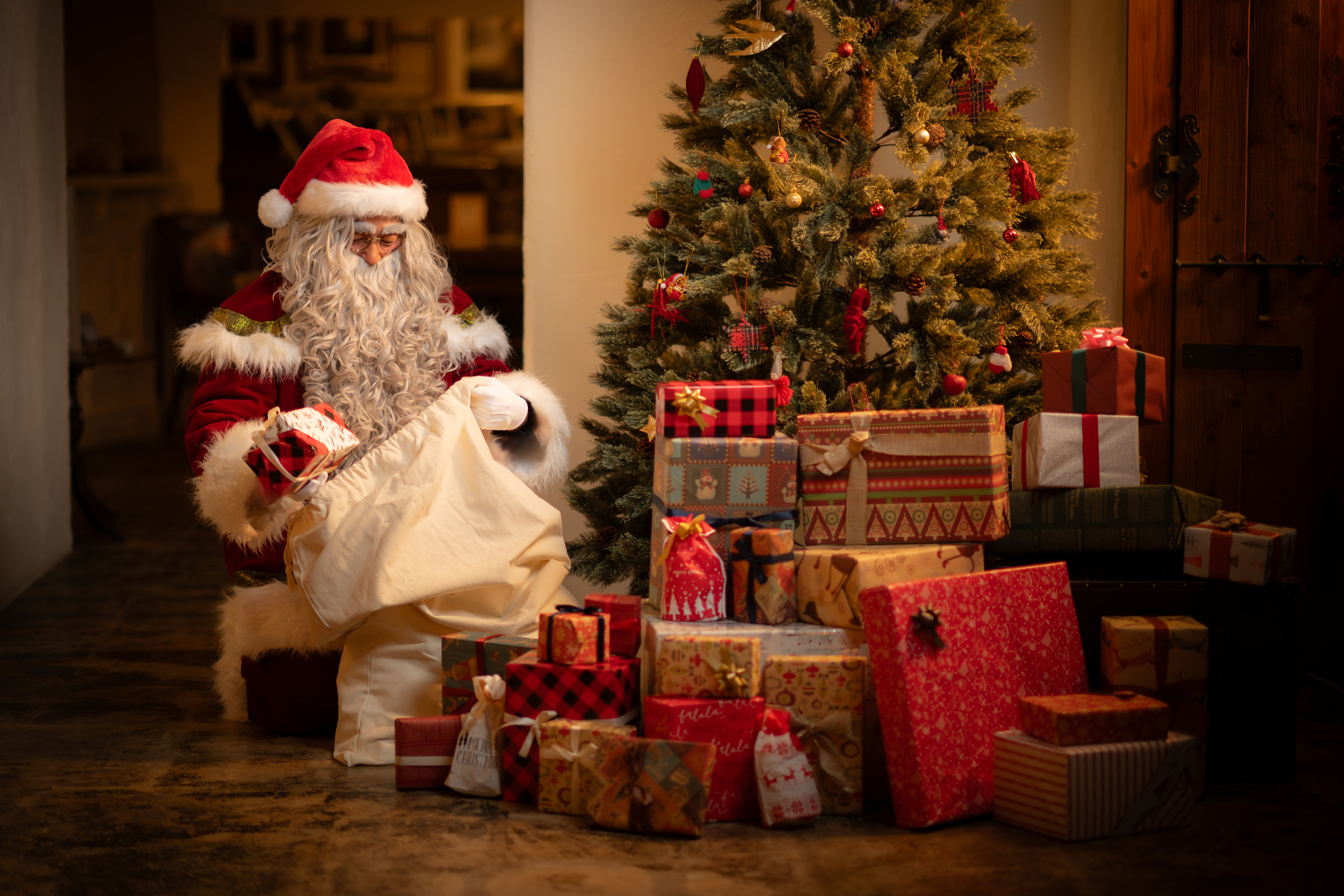 クリスマスツリーのそばで、白い袋からプレゼントを取り出すリアルサンタクロース（サンタ便）