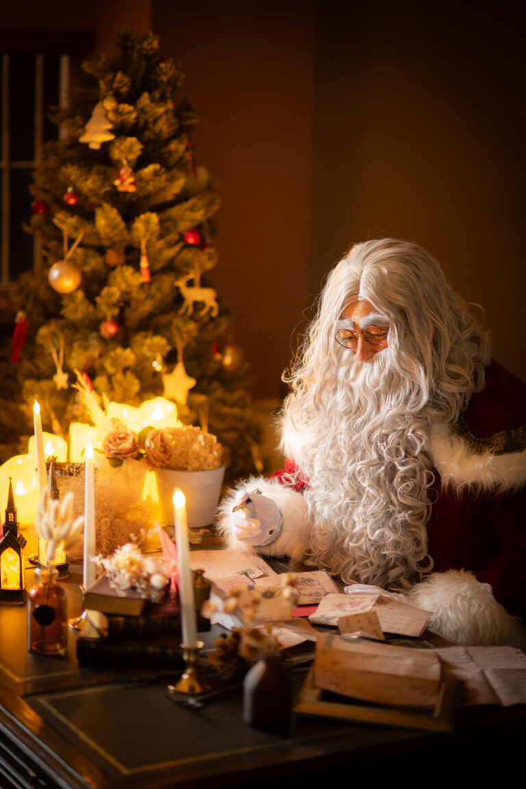 クリスマスツリーとキャンドルの灯りのそばで、机に向かうサンタクロース